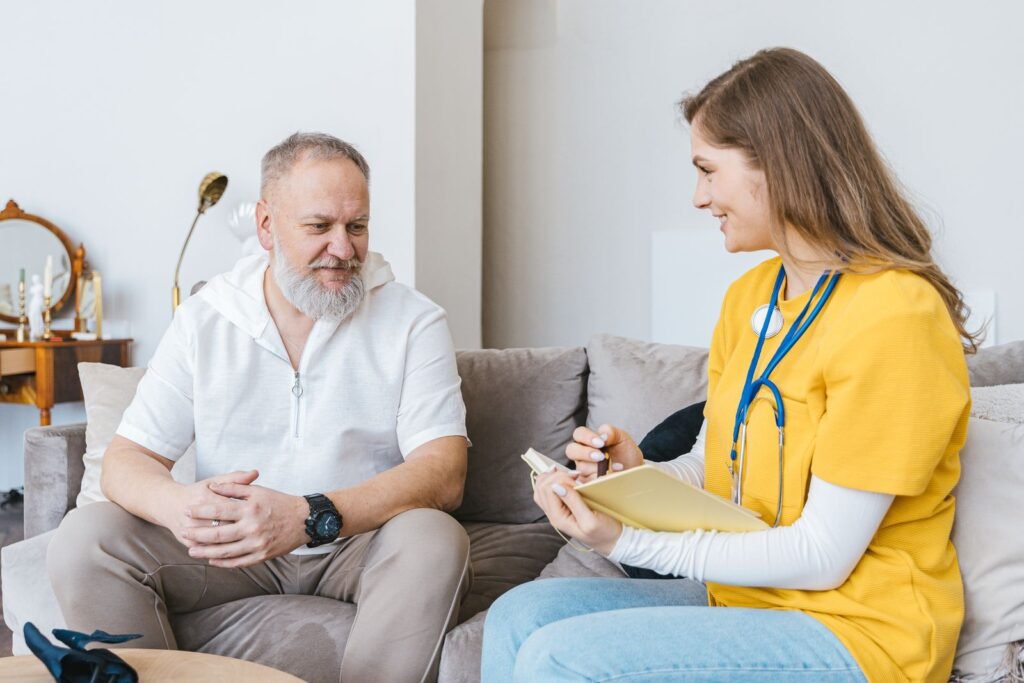 A caregiver talking with an older man in his bright living room